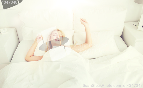 Image of young woman stretching in bed at home bedroom