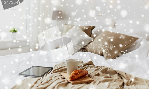 Image of tablet pc, coffee and croissant on bed at home