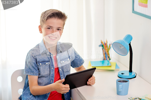 Image of smiling boy with tablet pc sitting at home desk