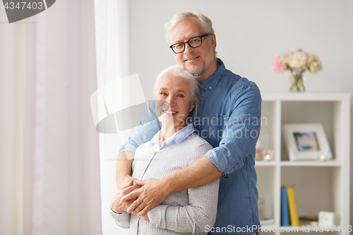 Image of happy senior couple hugging at home