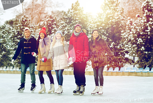 Image of happy friends ice skating on rink outdoors