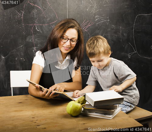 Image of little cute boy in glasses with young real teacher, classroom studying