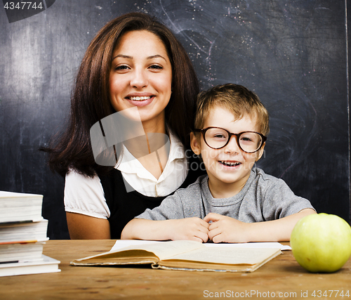 Image of little cute boy in glasses with young real teacher, classroom studying