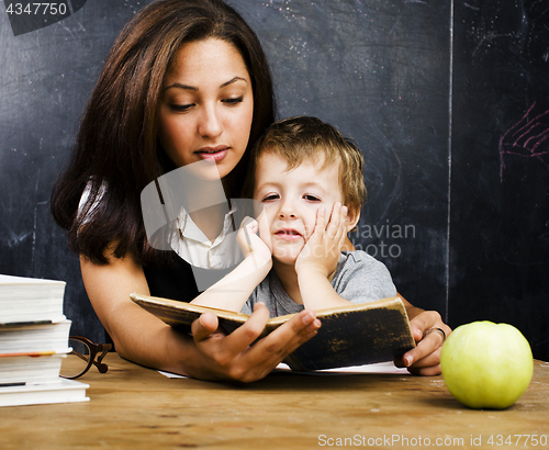 Image of little cute boy in glasses with young real teacher, classroom studying