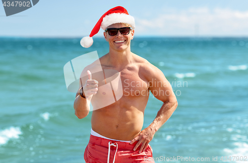 Image of happy man showing thumbs up on beach at christmas