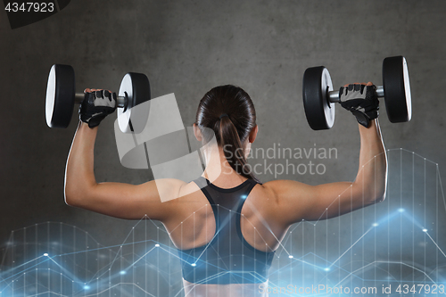 Image of young woman flexing muscles with dumbbells in gym