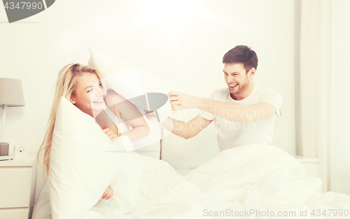 Image of happy couple having pillow fight in bed at home