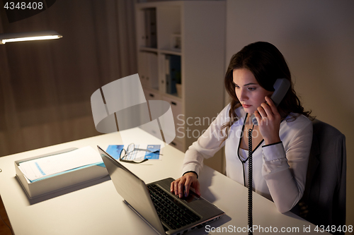 Image of woman with laptop calling on phone at night office