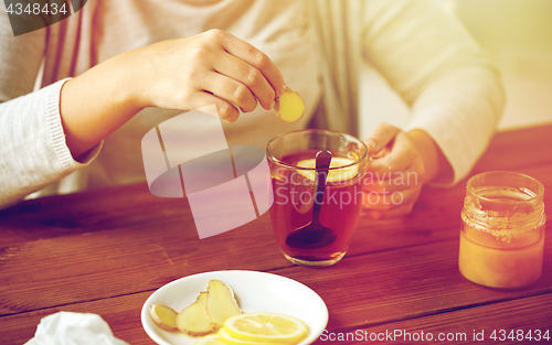 Image of close up of woman adding ginger to tea with lemon