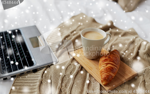 Image of laptop, coffee and croissant on bed at cozy home