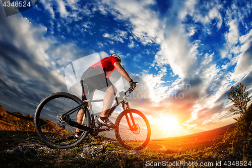 Image of cyclist standing with mountain bike on trail at sunset