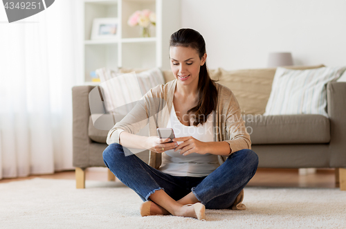 Image of happy woman texting message on smartphone at home