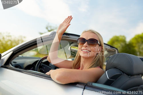 Image of happy young woman in convertible car waving hand