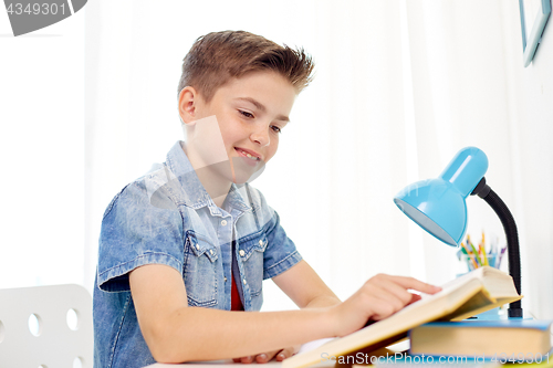 Image of student boy reading book at home table