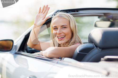 Image of happy young woman in convertible car waving hand