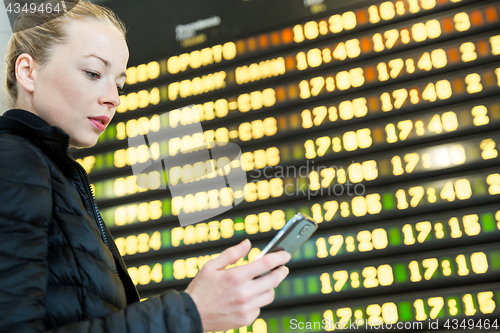 Image of Woman at airport in front of flight information board checking her phone.