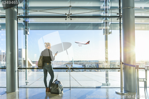 Image of Young woman waiting at airport, looking through the gate window.