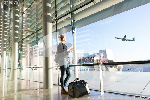 Image of Young woman waiting at airport, looking through the gate window.