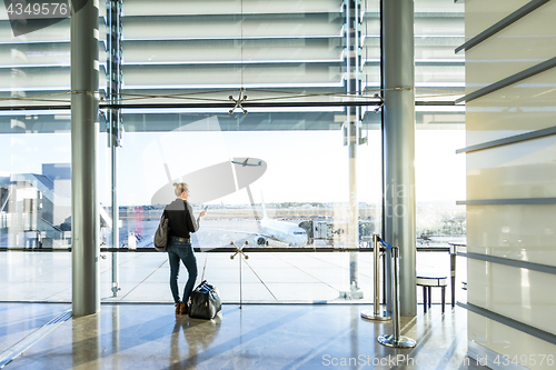 Image of Young woman waiting at airport, looking through the gate window.