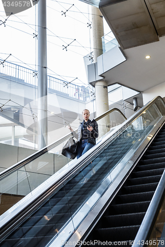 Image of Businesswoman with large black bag and mobile phone descending on escalator.