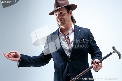 Image of The mature man in a suit and hat holding cane.