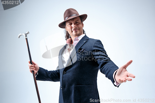 Image of The mature man in a suit and hat holding cane.