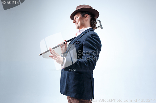 Image of The mature man in a suit and hat holding cane.