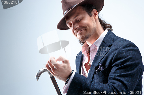 Image of The mature man in a suit and hat holding cane.