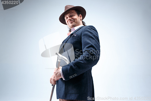 Image of The mature man in a suit and hat holding cane.