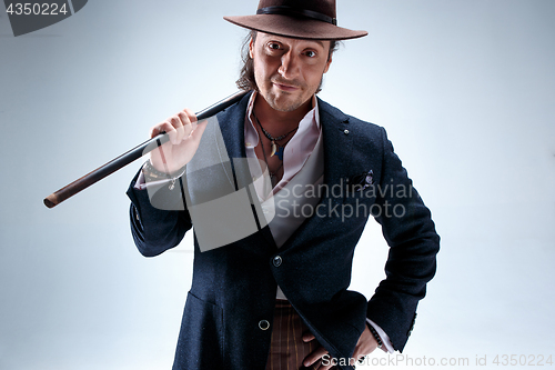 Image of The mature man in a suit and hat holding cane.