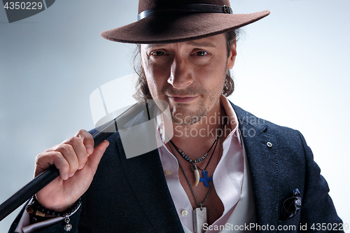 Image of The mature man in a suit and hat holding cane.