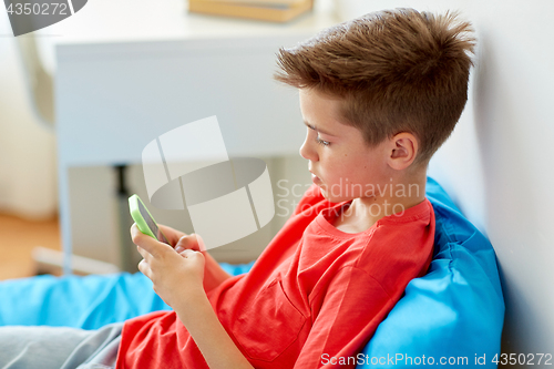 Image of boy with smartphone lying on bed at home