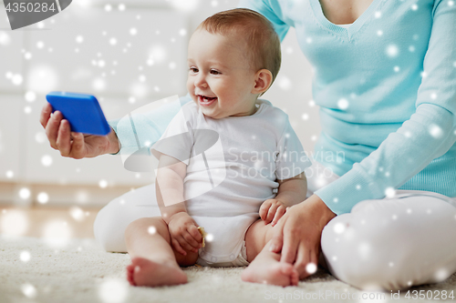 Image of happy mother showing smartphone to baby at home