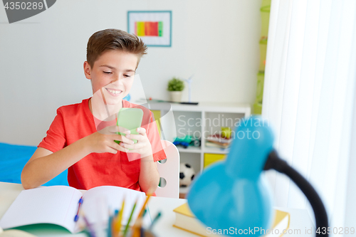 Image of student boy with smartphone distracting from study