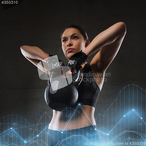 Image of young woman flexing muscles with kettlebell in gym