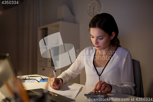 Image of woman with calculator and papers at night office