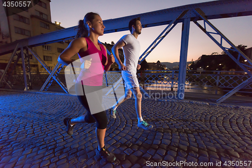 Image of couple jogging across the bridge in the city