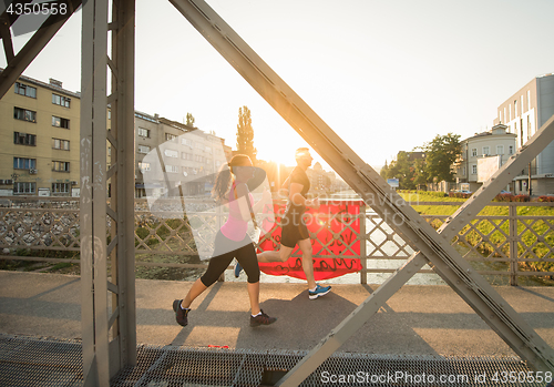 Image of young couple jogging across the bridge in the city