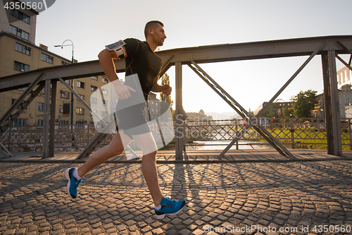 Image of man jogging across the bridge at sunny morning