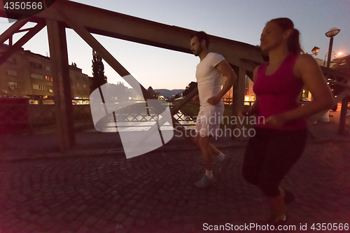 Image of couple jogging across the bridge in the city