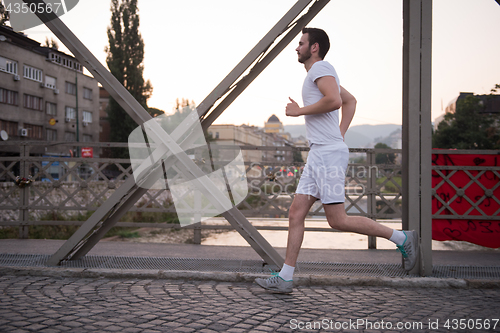 Image of man jogging across the bridge at sunny morning