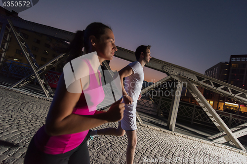 Image of couple jogging across the bridge in the city