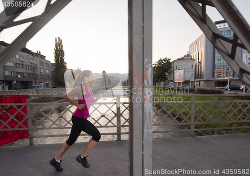 Image of woman jogging across the bridge at sunny morning