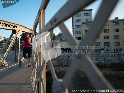 Image of woman jogging across the bridge at sunny morning