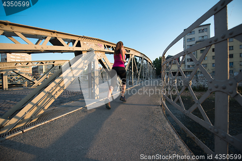 Image of woman jogging across the bridge at sunny morning