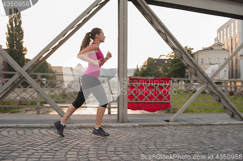 Image of woman jogging across the bridge at sunny morning