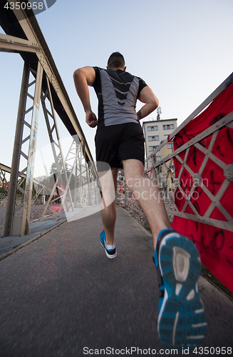 Image of man jogging across the bridge at sunny morning