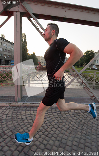 Image of man jogging across the bridge at sunny morning