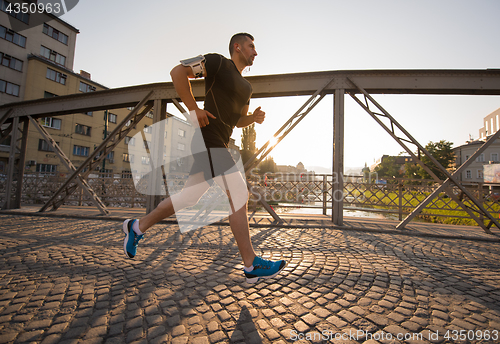 Image of man jogging across the bridge at sunny morning