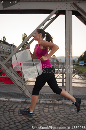 Image of woman jogging across the bridge at sunny morning